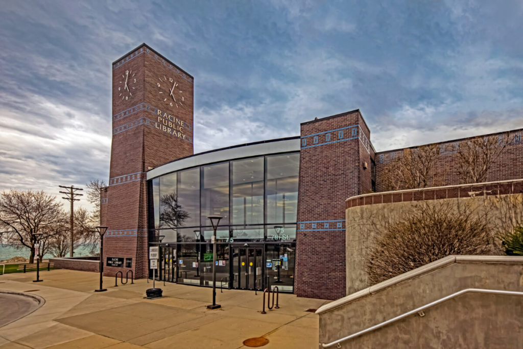 The library as seen from the steps leading to Lake Avenue. From this angle, you can see the the glass windows and doors opening into the lobby, encased by the clock tower on the left and a thick pillar on the right. Other than the glass, the library is made of dark red brick with blue tile accents.
