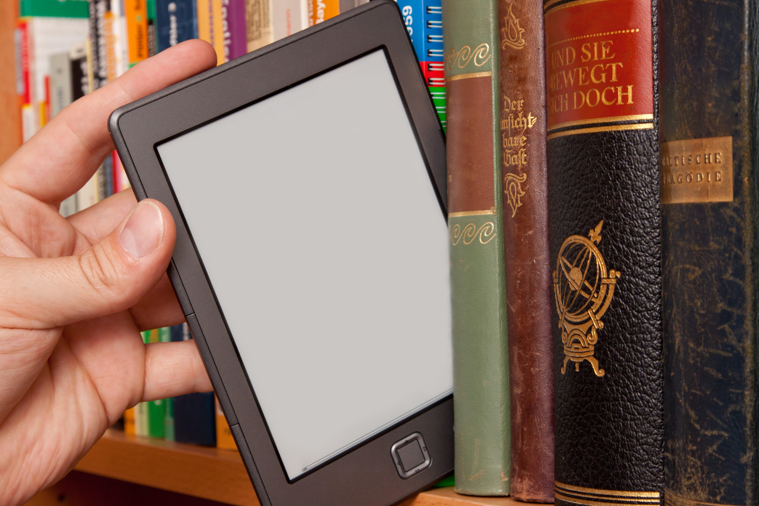 A hand pulls an e-reader out from amidst a shelf of books.