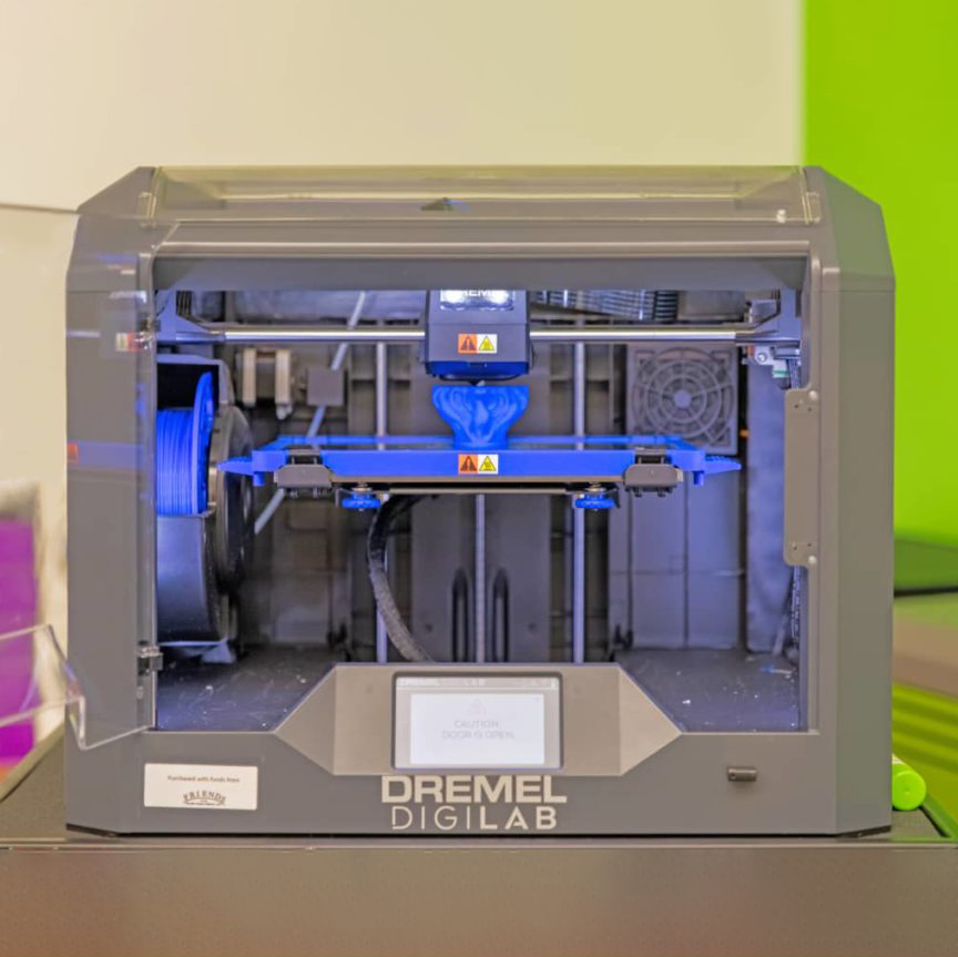 A photo of the library's Dremel DigiLab 3D printer, a metal box with a plastic front panel opened for access to the interior compartment containing print filament, machinery and a fan.