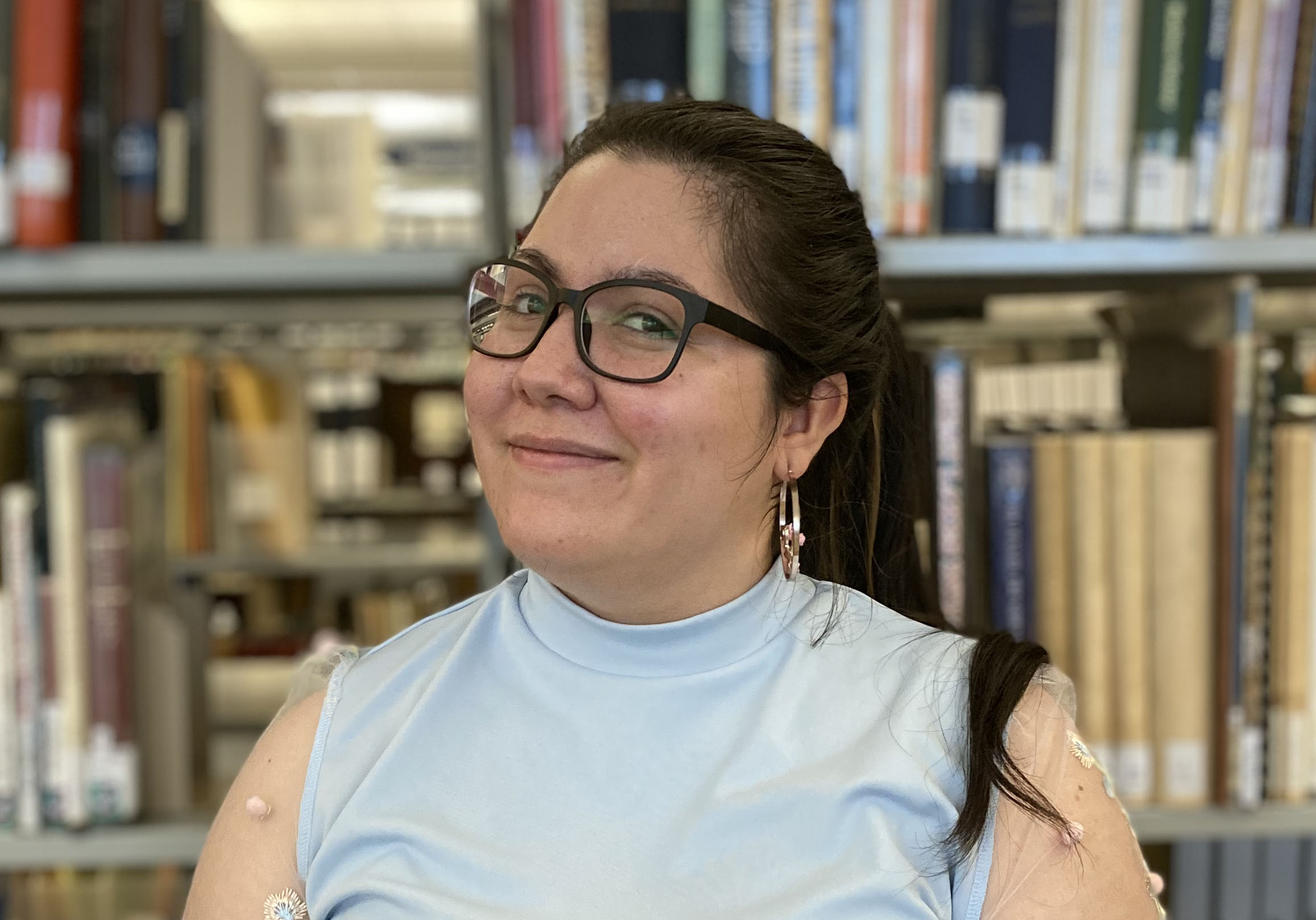 A photo of Shay King, a straight-sized, whiteish, nonbinary person with big glasses and long, black hair pulled back in a ponytail.