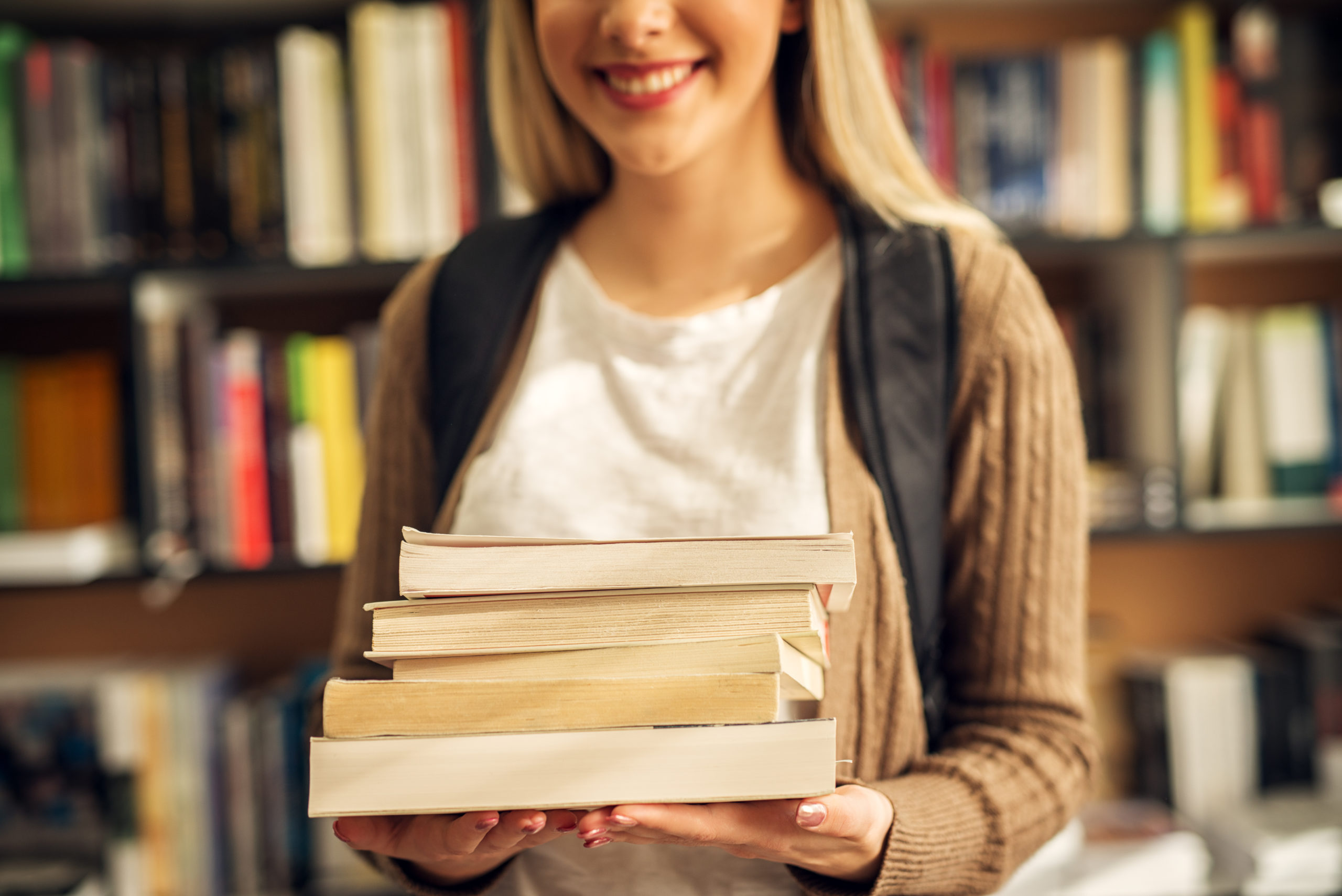 A person holds a pile of four books and smiles. 