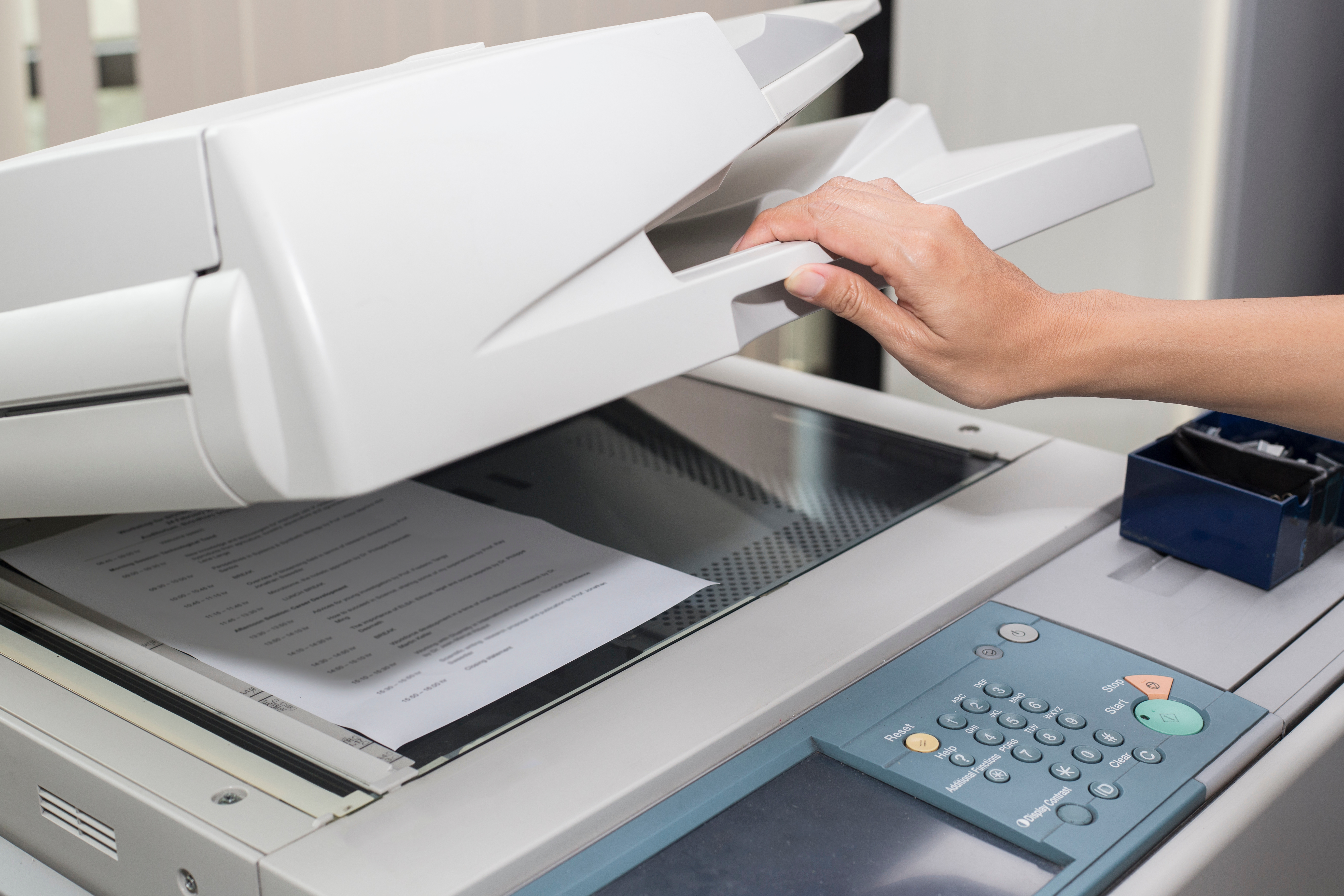 A person closes a copier with a document on it, ready to scan.