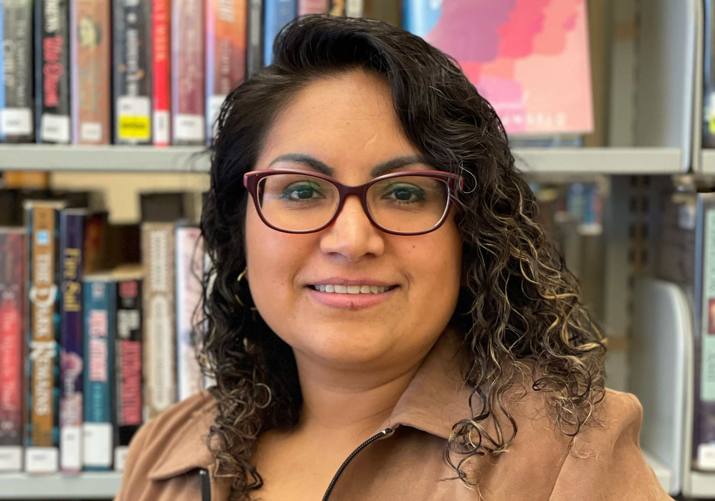 A photo of a library staff member: Business Manager Evelin Garcia, a Latinx woman with long, dark curly hair and rectangular brown glasses.