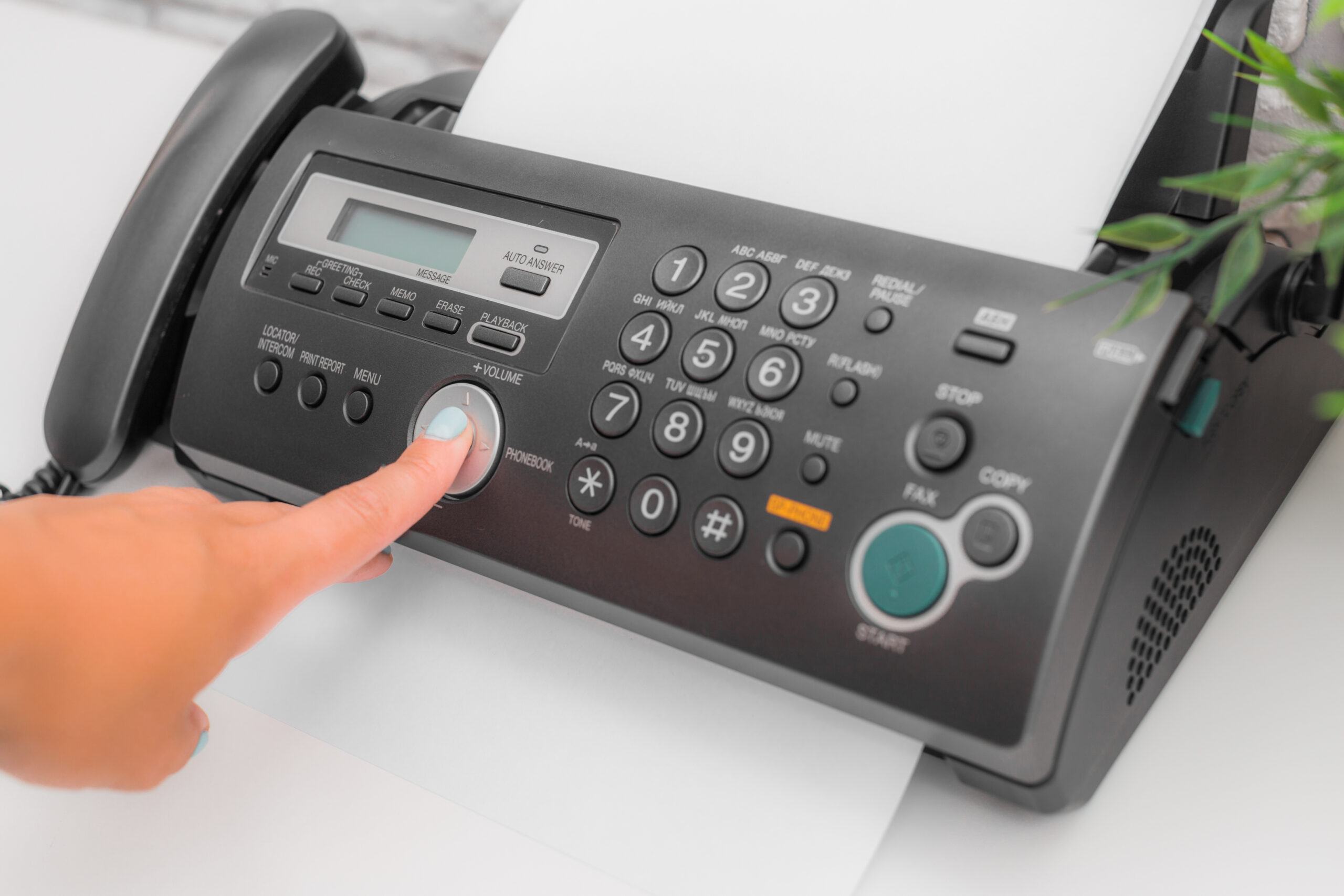 A person presses the button on a fax machine, loaded up to send correspondence out.