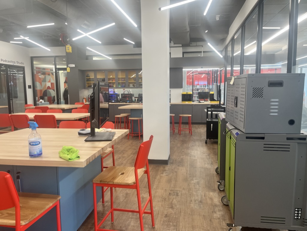 The renovated Innovation Lab, a room full of stations with tables and chairs where users can try robots, learn to code and more. You can see cabinets full of tech and countertops lined with 3D printers and laser engravers throughout the room.