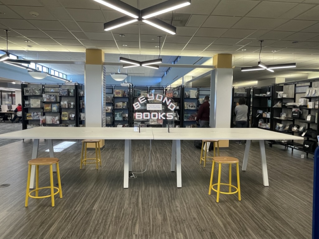 A photo of the Racine Public Library's Beyond Books Collection. The collection consists of an L-shaped wall of shelves full of board games, tools, hobby supplies, and more.