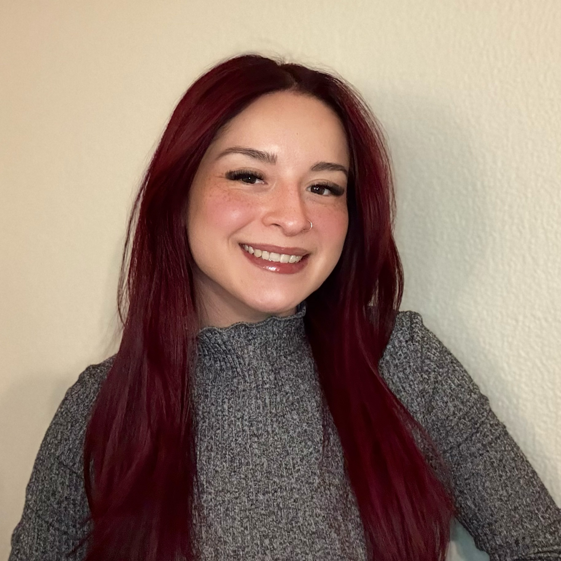 25-12 Ashley Cedeño Headshot - square A photo of a library staff member: Social Worker Ashley Cedeño, a Latinx woman with straight, dark red hair past her shoulders.